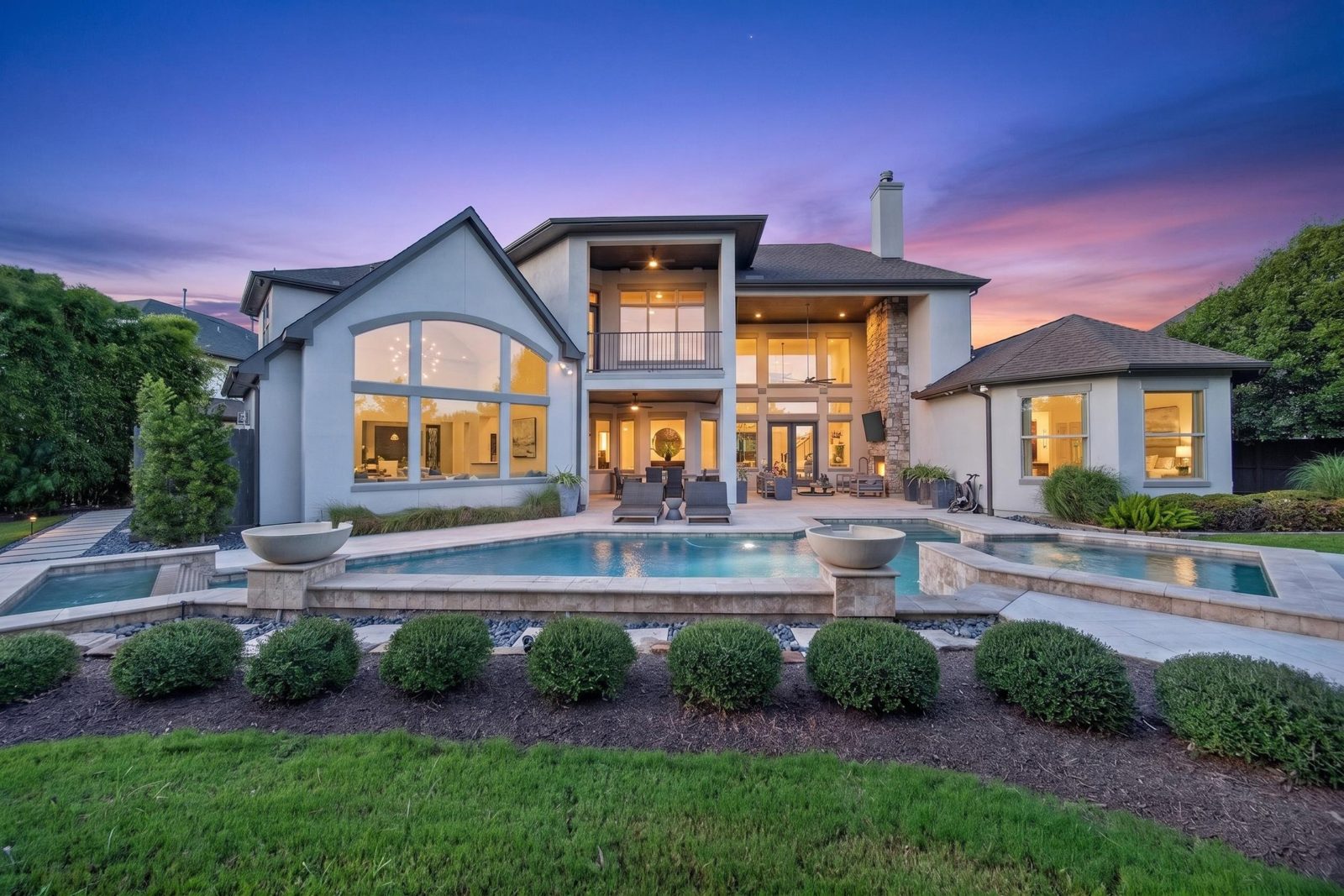 Luxury home and pool at sunset with warm lights in every window